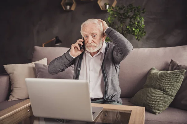 Photo of impressed old man dressed white shirt sitting sofa looking modern device having call indoors flat home house — Stock Photo, Image