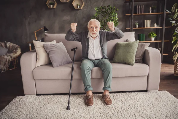 Fénykép dühös öregember öltözött fehér ing ül kanapé emelkedő öklök beltéri lakás — Stock Fotó