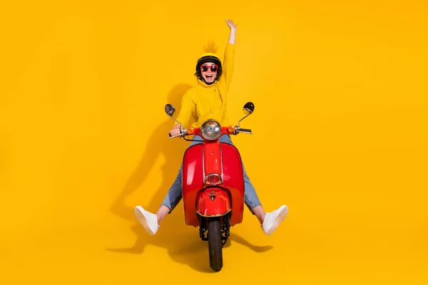 Retrato fotográfico de una chica alegre levantando una mano montando un ciclomotor retro rojo aislado sobre un fondo de color amarillo vivo — Foto de Stock