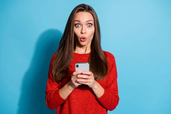 Здивована дівчина використовує смартфон в соціальних мережах інформаційний одяг пуловер ізольований синій колір фону — стокове фото