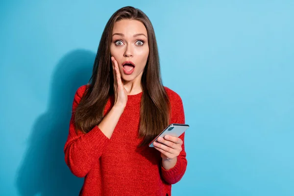 Fotografie užaslé dívky použití smartphone dotykové ruce křičí nosit pulovr izolované přes modré barvy pozadí — Stock fotografie