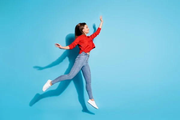 フルサイズの写真の面白い女性ジャンプアップ良い気分を着用ニット赤プルオーバースニーカージーンズ隔離された青の色の背景 — ストック写真
