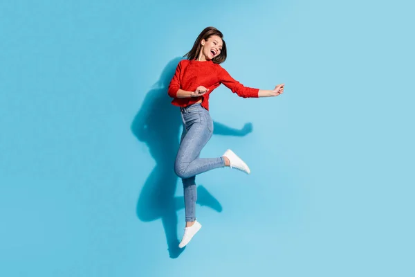 Teljes méretű fotó vicces hölgy ugrás magas öröm viselet kötött piros pulóver tornacipő farmer elszigetelt kék szín háttér — Stock Fotó