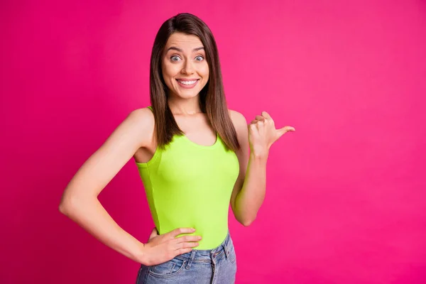 Foto de chica joven excitada indican pulgar vacío espacio brillante sonrisa de dientes usar verde superior aislado color rosa vivo fondo —  Fotos de Stock