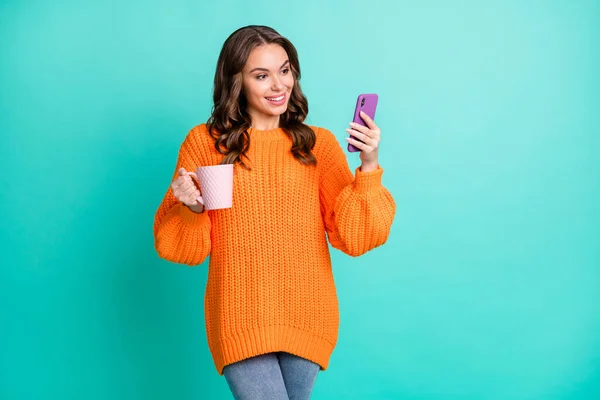 Фотографія молодої красивої привабливої щасливої усміхненої дівчини п'є чай за допомогою смартфона ізольовано на бірюзовому кольоровому фоні — стокове фото