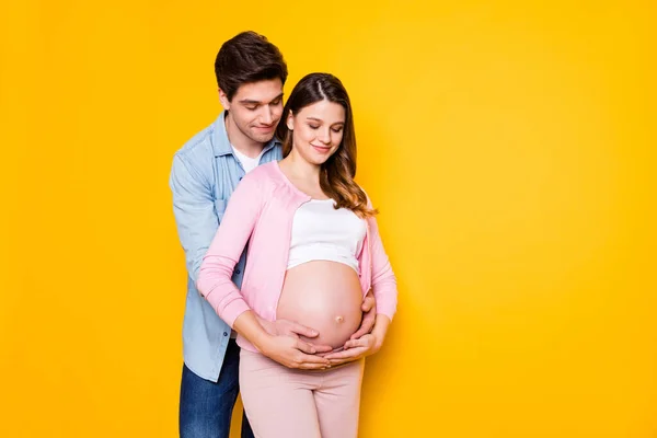 年轻夫妇站在一起拥抱孕妇的照片，身穿休闲装，与黄色背景隔离 — 图库照片