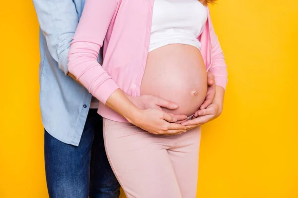 年轻夫妇站在一起拥抱孕妇的照片。孕妇身穿休闲装，背景是黄色的 — 图库照片