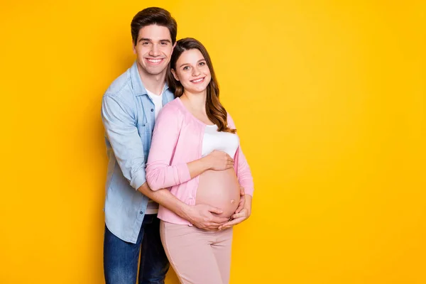 Foto de jovem casal stand abraço mulher grávida usar roupas casuais isolado no fundo de cor amarela — Fotografia de Stock