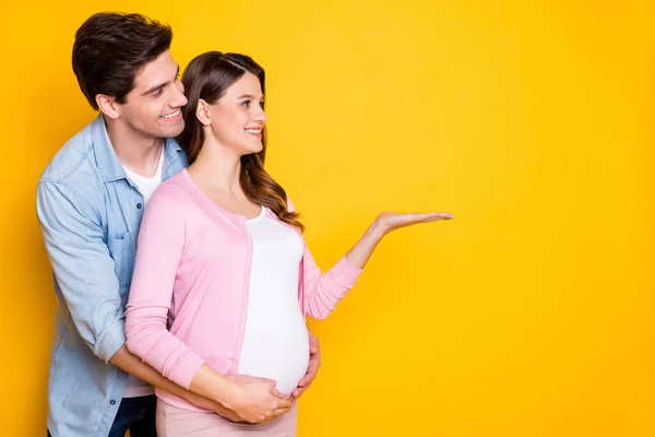 Profile photo of young couple stand hug pregnant woman hold empty space wear casual outfits isolated on yellow color background — Stock Photo, Image