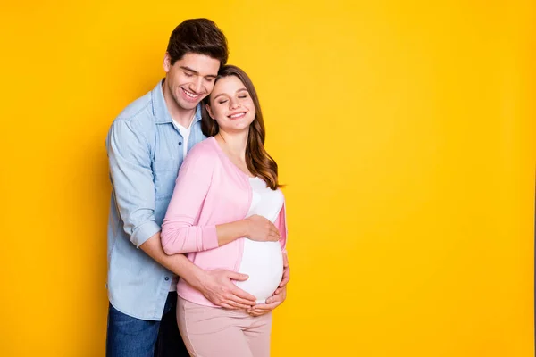 Foto de casal jovem olhos fechados stand abraço mulher grávida usar roupas casuais isolado no fundo de cor amarela — Fotografia de Stock
