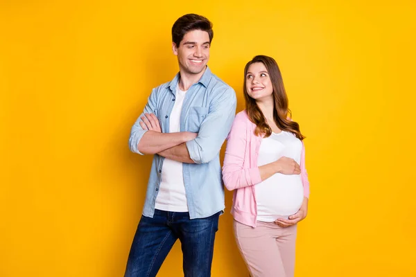 Foto de casal atraente esperando criança pai braços dobrados mamãe abraçando barriga olhando uns para os outros isolado cor amarela fundo — Fotografia de Stock