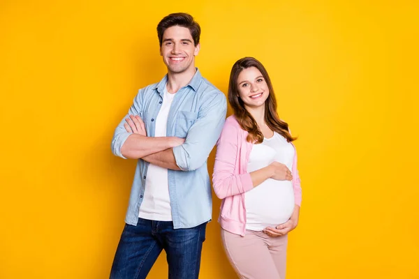 Foto de bela família esperando bebê mamãe abraçando barriga pai braços cruzados isolado cor amarela fundo — Fotografia de Stock