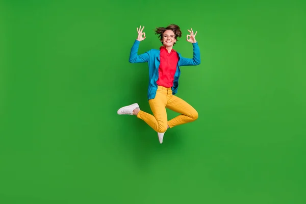 Ganzkörpergröße Foto von glücklichen Mädchen springen hoch zeigt okay Zeichen lächeln isoliert auf lebendigen grünen Farbhintergrund — Stockfoto