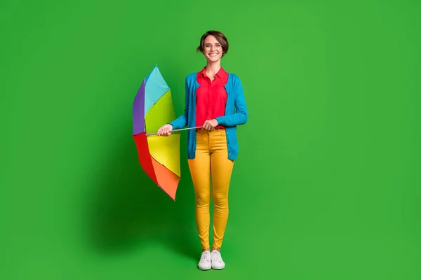 Фотографія повного розміру тіла позитивної дівчини в окулярах, що тримає барвисту парасольку, усміхнену ізольовану на яскраво-зеленому кольоровому фоні — стокове фото