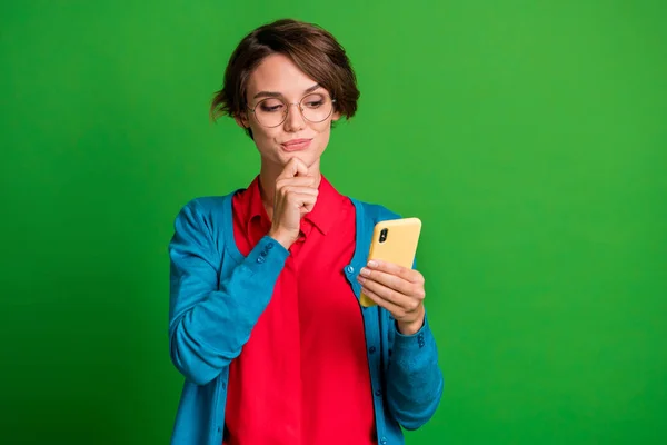 똑똑하고 생각깊은 여자가 스마트폰으로 정보를 읽는 사진, 선명 한 녹색 배경에 턱을 만진 사진 — 스톡 사진