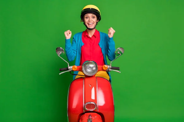 Zdjęcie młodego wesoły uśmiech podekscytowany dobry nastrój dziewczyna trzymać pięści w zwycięstwie jeździć czerwony motorower odizolowany na zielonym tle kolor — Zdjęcie stockowe