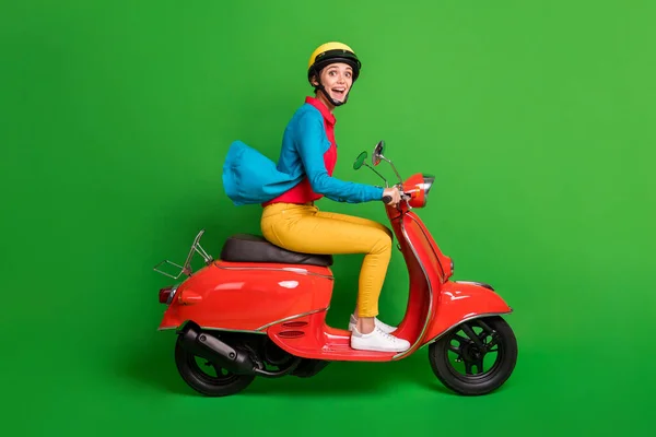 Full size profile side photo of young excited happy joyful girl look camera ride red motorcycle isolated on green color background