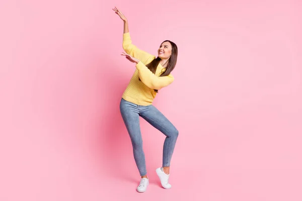 Foto de tamaño completo de joven atractivo sonriente alegre buen humor chica bailando mirada en las manos aisladas en el fondo de color rosa —  Fotos de Stock