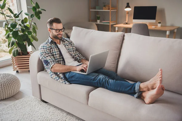 Foto lateral de perfil de cuerpo completo de joven hombre alegre sentarse sofá hogar trabajo distancia programador tipo email ordenador portátil —  Fotos de Stock