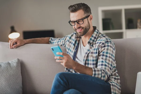 Foto de joven alegre hombre feliz sonrisa positiva leer navegar por Internet teléfono celular chat tipo sms sentarse sofá interior — Foto de Stock