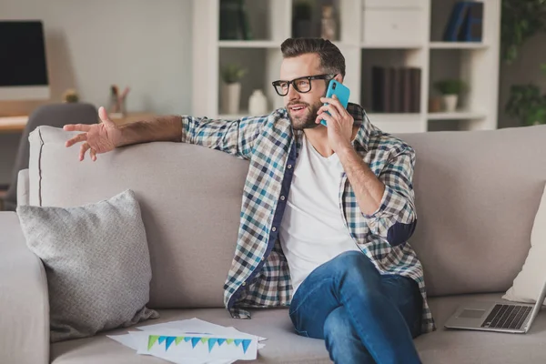 Foto do jovem homem bonito sentar sofá casa conforto feliz sorriso chamada falar celular olhar espaço vazio — Fotografia de Stock