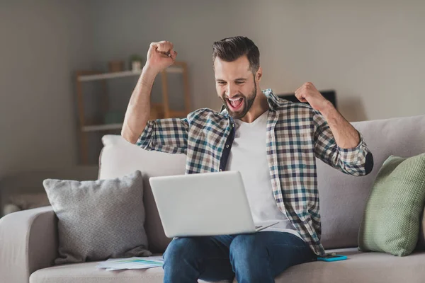 Photo de jeune homme excité heureux sourire positif assis canapé maison regarder ordinateur portable célébrer victoire succès poings mains — Photo