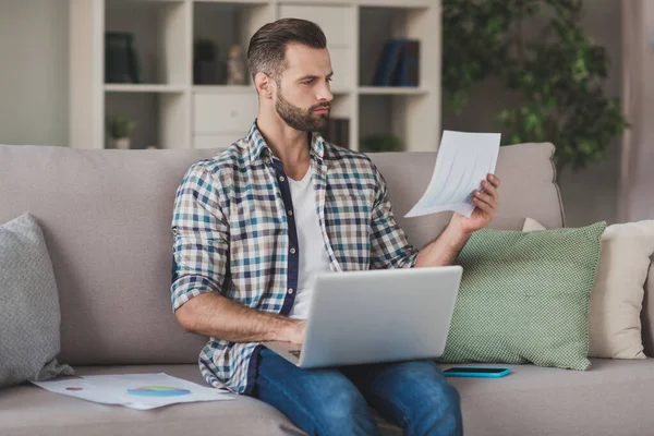 Profil sida foto av ung stilig affärsman allvarlig look dokument fjärrarbete laptop sitta soffa hem — Stockfoto