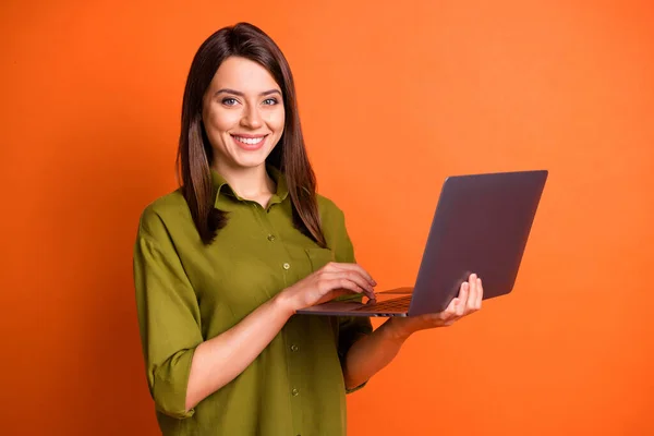 Фотопортрет молодой женщины-фрилансера с помощью пальцев ноутбука на тачпаде, улыбающейся изолированно на ярко-оранжевом фоне — стоковое фото