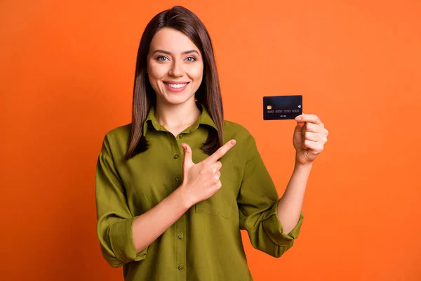 Foto porträtt av ung flicka pekar på bank plast kort isolerad på ljusa orange färg bakgrund — Stockfoto