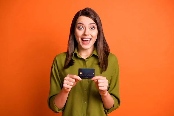 Foto de chica impactada funky sostener tarjeta de plástico mirar cámara boca abierta usar camisa verde aislado color naranja fondo — Foto de Stock