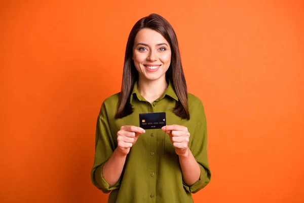 Foto de chica positiva alegre mantenga tarjeta de crédito sonrisa dental desgaste camisa verde aislado color naranja fondo — Foto de Stock