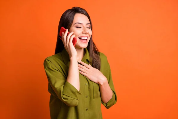 Profil fotó vicces fiatal lány hold smartphone csukott szemmel kéz mellkas viselet zöld ing elszigetelt narancs szín háttér — Stock Fotó
