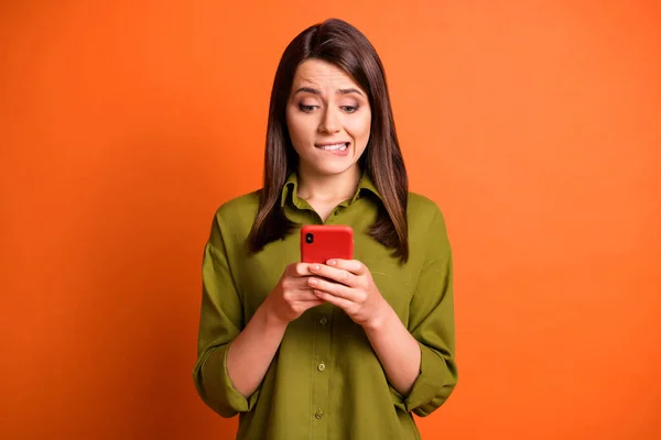 Foto van bang jong meisje houden telefoon beet lip look scherm dragen groen shirt geïsoleerde oranje kleur achtergrond — Stockfoto