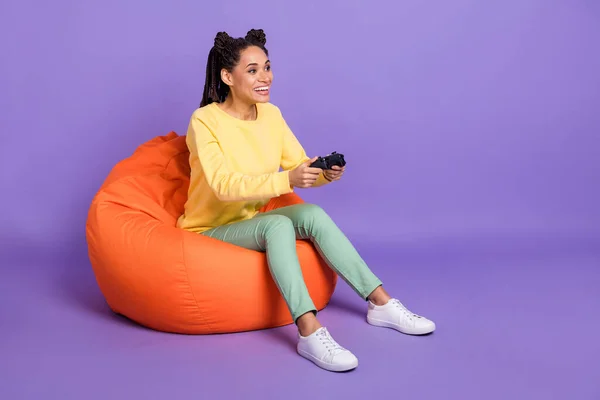 Pełny rozmiar zdjęcie optymistycznej dziewczyny siedzieć na puf Playstation nosić żółtą koszulę trampki izolowane na tle koloru liliowego — Zdjęcie stockowe
