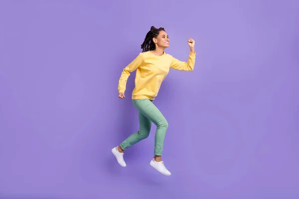 Foto de perfil de tamaño completo de niña optimista salto usar pantalones de camisa amarilla zapatillas aisladas sobre fondo de color lila — Foto de Stock