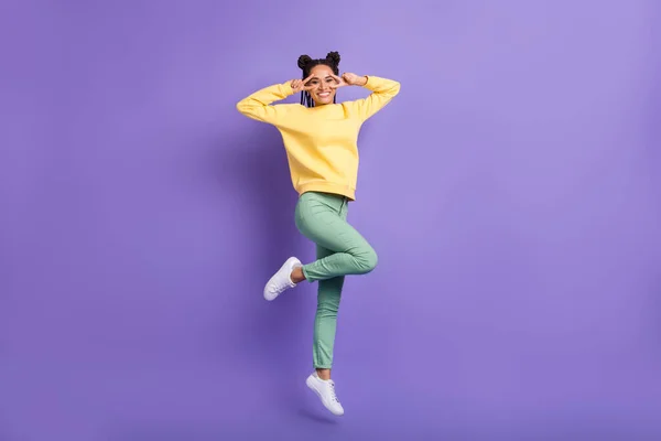 Full size profile photo of optimistic girl jump show v-sign wear yellow shirt trousers sneakers isolated on lilac color background — Stock Photo, Image