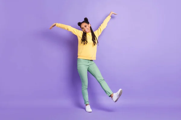 Foto de tamaño completo de optimista agradable dama manos arriba usar suéter amarillo pantalones zapatillas aisladas sobre fondo de color lila — Foto de Stock