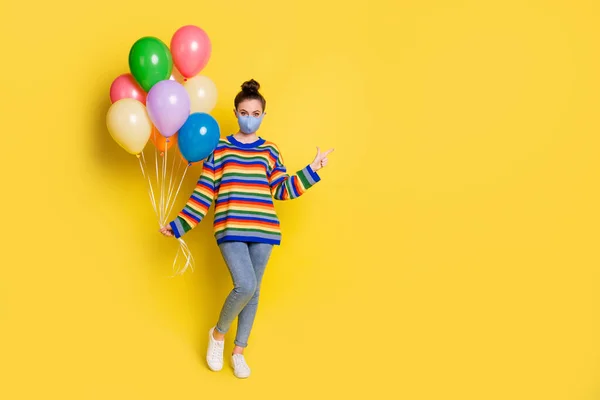 Hava balonları tutan genç kızın tam boy fotoğrafı tıbbi maske nokta işaret parmağı takıyor sarı arka planda izole edilmiş boş bir yer. — Stok fotoğraf