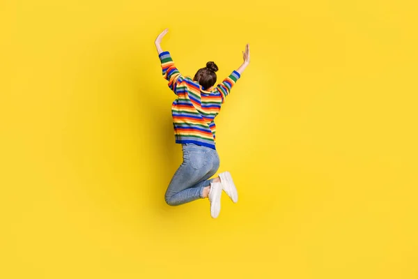 Full størrelse bakover i ryggsøylen, foto av en pen jente som hopper opp i luften, hever hendene, går med regnbuefarget genser isolert på livaktig bakgrunn – stockfoto
