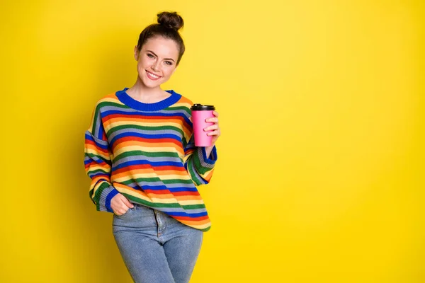 Photo of nice optimistic brunette girl stand hold cup hand in pocket wear rainbow sweater blue pants isolated on bright yellow background — Stock Photo, Image