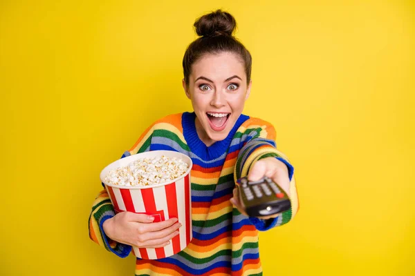 Porträtt av ganska söt brunett flicka äter popcorn hålla fjärrkontroll bära regnbåge tröja isolerad på ljust gul bakgrund — Stockfoto