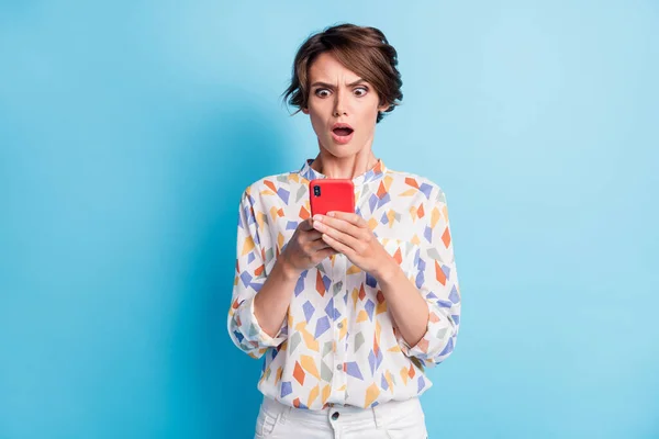 Mutsuz, şok olmuş genç bir kadının fotoğrafı mavi arkaplanda izole edilmiş telefon bildirimine bakın. — Stok fotoğraf