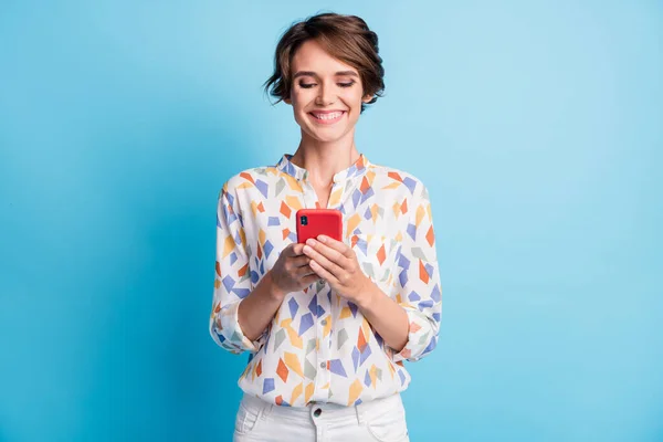 Фото очаровательной милой молодой леди смотреть держать смартфон носить белый отпечаток рубашки изолированы на синем фоне — стоковое фото
