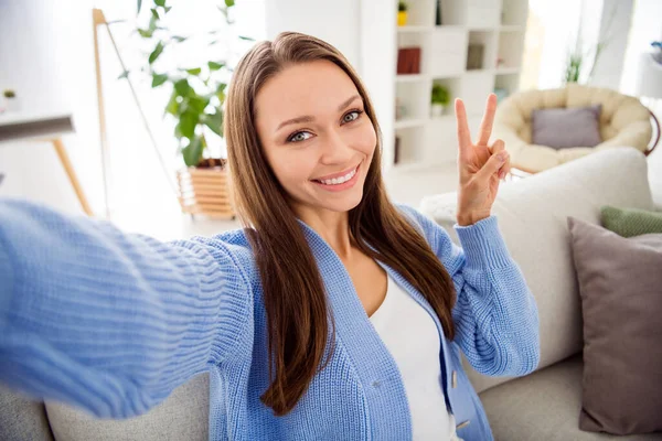 Autorretrato de atractiva chica alegre sentado en diván mostrando v-signo de tiempo libre en la luz plana casa apartamento sala de estar interior — Foto de Stock