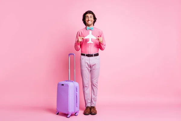 Corpo inteiro foto de homem morena bonito usar calça azul bowtie violeta bagagem segurar avião de papel isolado no fundo cor-de-rosa — Fotografia de Stock