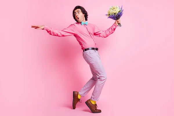 Full size προφίλ πλευρά φωτογραφία του funky καστανά μαλλιά άνθρωπος κοιτάξουμε πίσω κρατήσει τα λουλούδια χέρι φορούν μπλε παπιγιόν πάει απομονωθεί σε ροζ φόντο χρώμα — Φωτογραφία Αρχείου