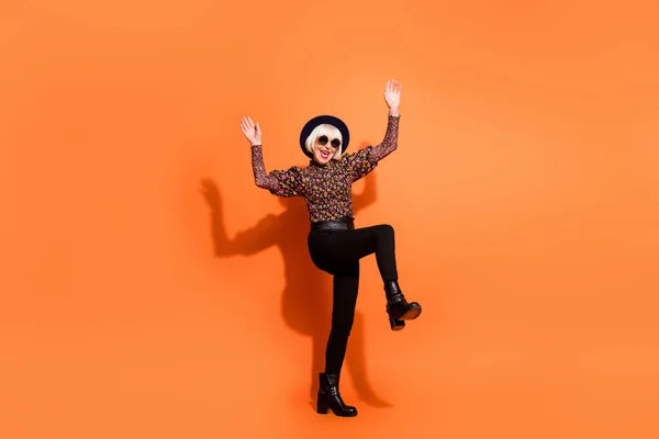 Foto de tamaño completo de viejo funky sonriente alegre dama positiva en gafas de sol bailando levantar las manos pierna aislada sobre fondo de color naranja —  Fotos de Stock