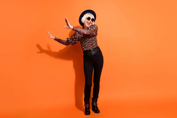 Foto de tamaño completo de loco sonriente emocionado feliz señora bailando desgaste pantalones negros y gafas aisladas en fondo de color naranja —  Fotos de Stock