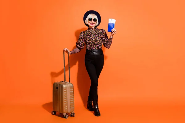 Full size foto van vrolijke positieve goede humeur oude dame tonen tickets paspoort ruim bagage geïsoleerd op oranje kleur achtergrond — Stockfoto