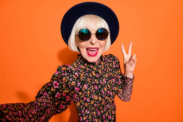 Portret van oude glimlachende funky gekke positieve goede humeur dame nemen selfie tonen v-teken geïsoleerd op oranje kleur achtergrond — Stockfoto